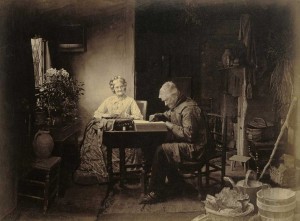 Elderly couple sitting at a table. She is darning socks; he is reading.